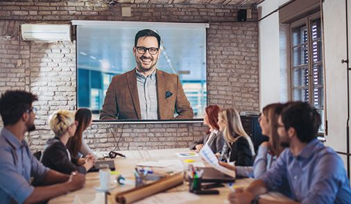 Professionals sitting in a large conference room and videoconferencing with a large projection screen