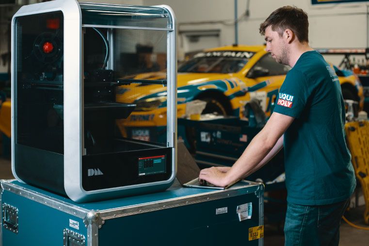 man standing in front of the Desktop Metal composite 3D printer in an automotive shop