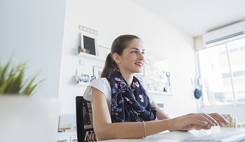 Working woman smiling while sitting at computer with her hands placed on mouse and keyboard in an in an ergonomic fashion