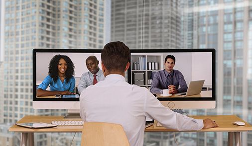 Man video-conferencing on two separate monitors from a huddle space