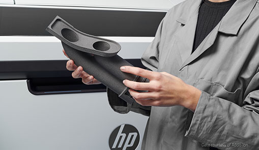 A woman positioned in front of an HP 3D printer holding a 3D printed automotive part