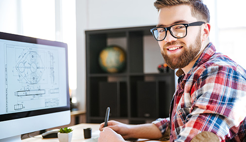 Man smiling at camera as he sits in front of his office computer, representing Secure Supply Chain Management and Device Security